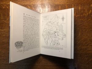 Image of a book lying open in a cradle, the right hand page is illustrated with a map