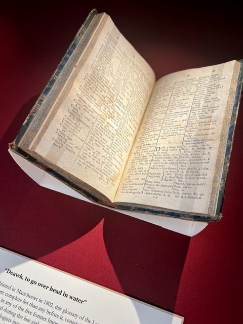 Photograph of a glossary of Lancashire dialect, mounted in a cradle so the pages are open, against a red background.