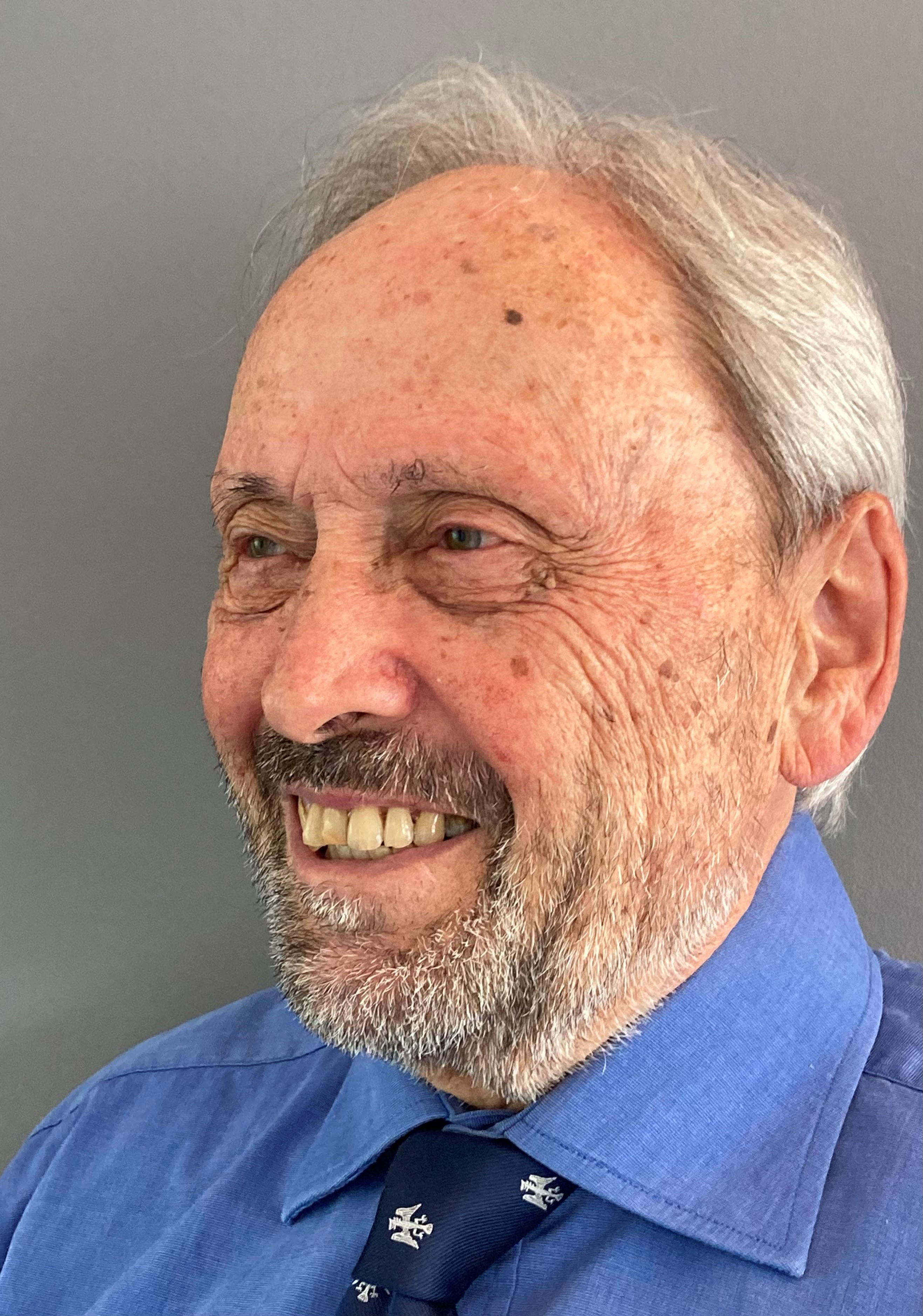 Sir Brian Donnelly profile photo. Sir Brian wears a blue shirt and tie and is smiling.