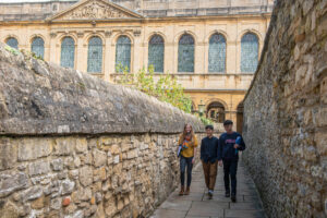 three students walking along Long Walls with library in the background