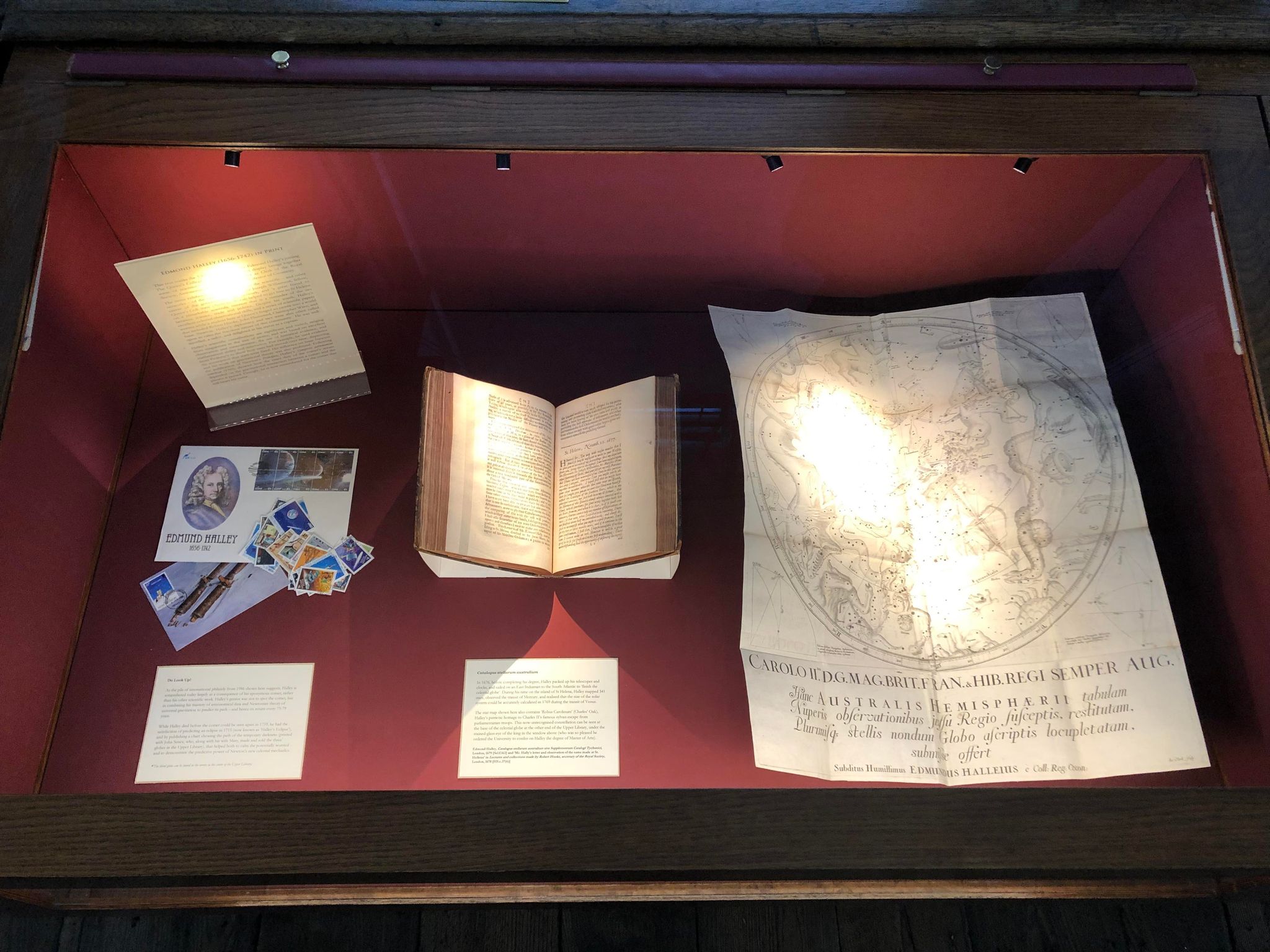 An exhibition case containing ephemera, a mounted book and a large celestial map, plus captions