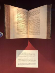 Photograph of an open copy of 'Lectures and collections made by Robert Hooke' showing ‘Mr. Hally’s letter and observation of the same made at St. Hellena’. A text panel is below to caption the displayed item. The background is red fabric.