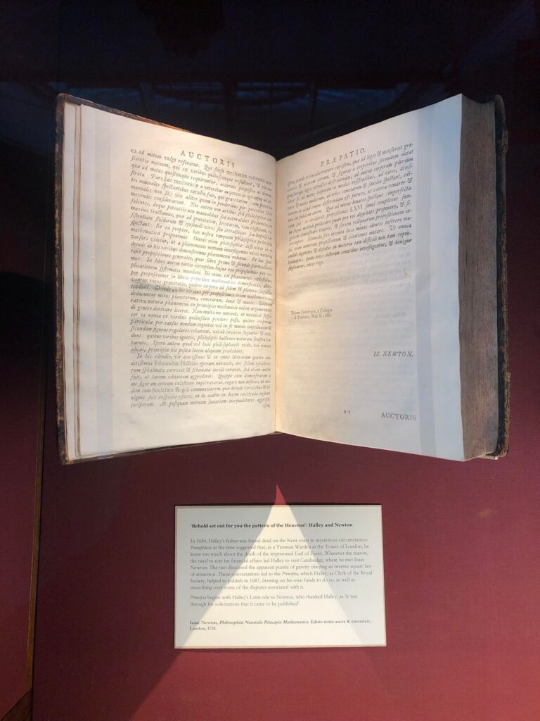 A copy of Isaac Newton's Principia open, with a panel of text below