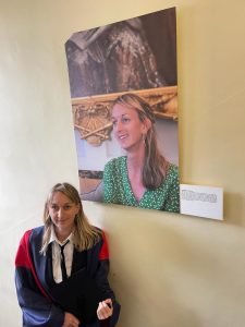April Burt in graduation gowns next to her portrait from the Shining a Light exhibition