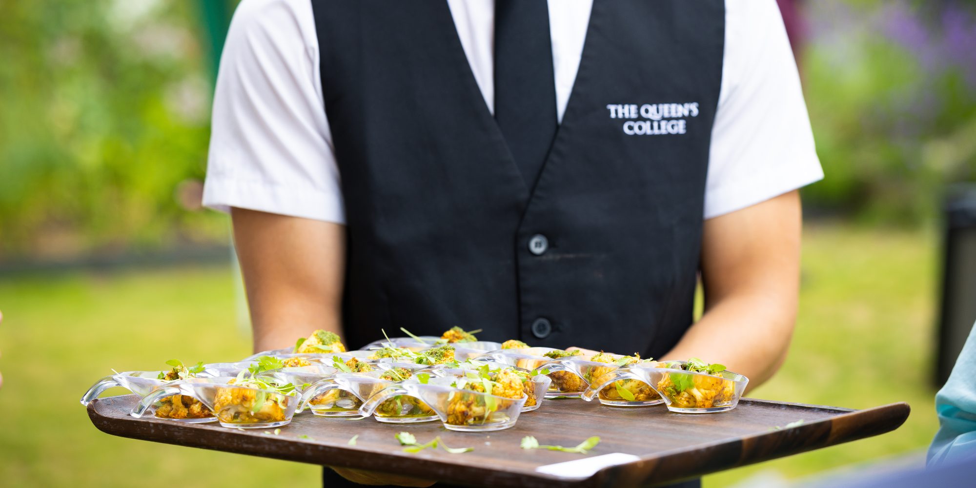 a waiter wearing a black waistcoat holding a tray of canapes