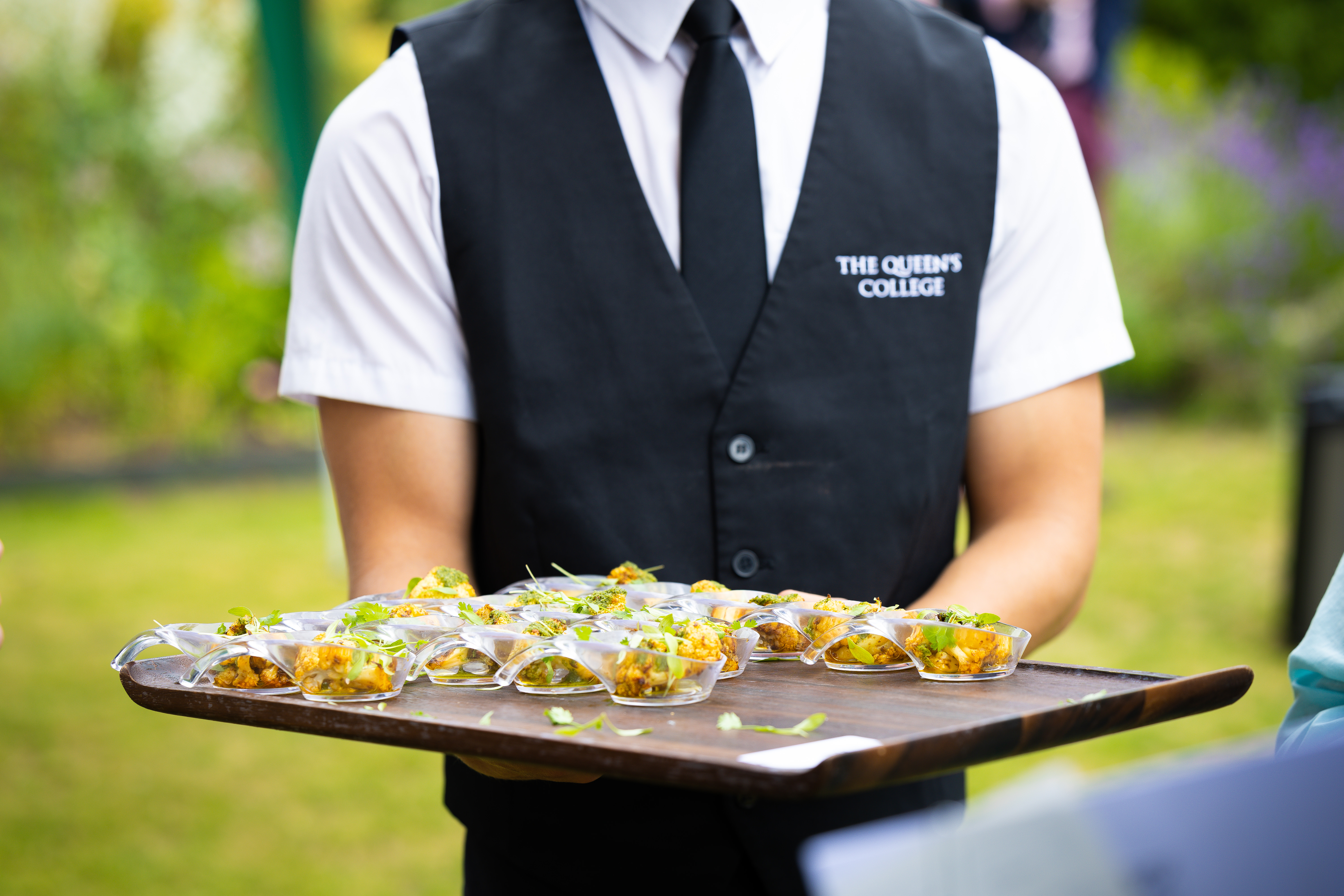 a waiter wearing a black waistcoat holding a tray of canapes