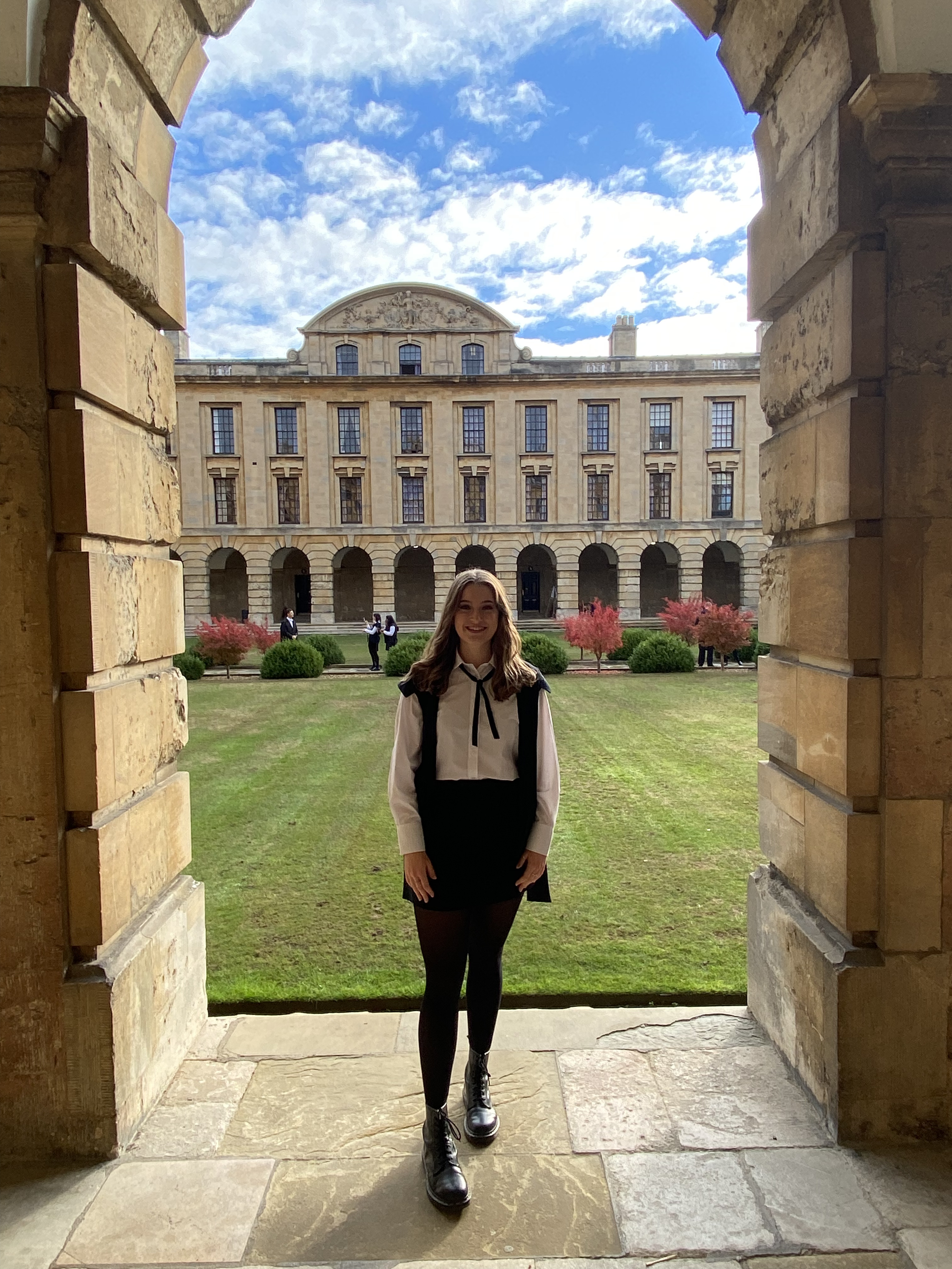 Megan wearing subfusc standing in the cloister with the Front Quad behind her