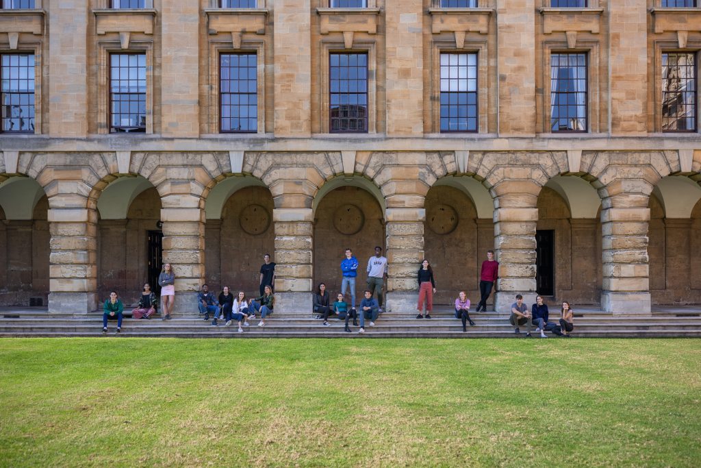 Front Quad at Queen's with a group of students standing in the cloister looking across the lawn to the camera