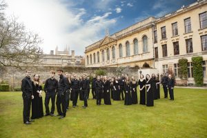 The Choir of The Queen's College standing in the Fellows' Garden with the library in the background