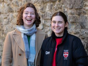 Bryony and Dani pictured together against the stone walls in the Fellows' Garden