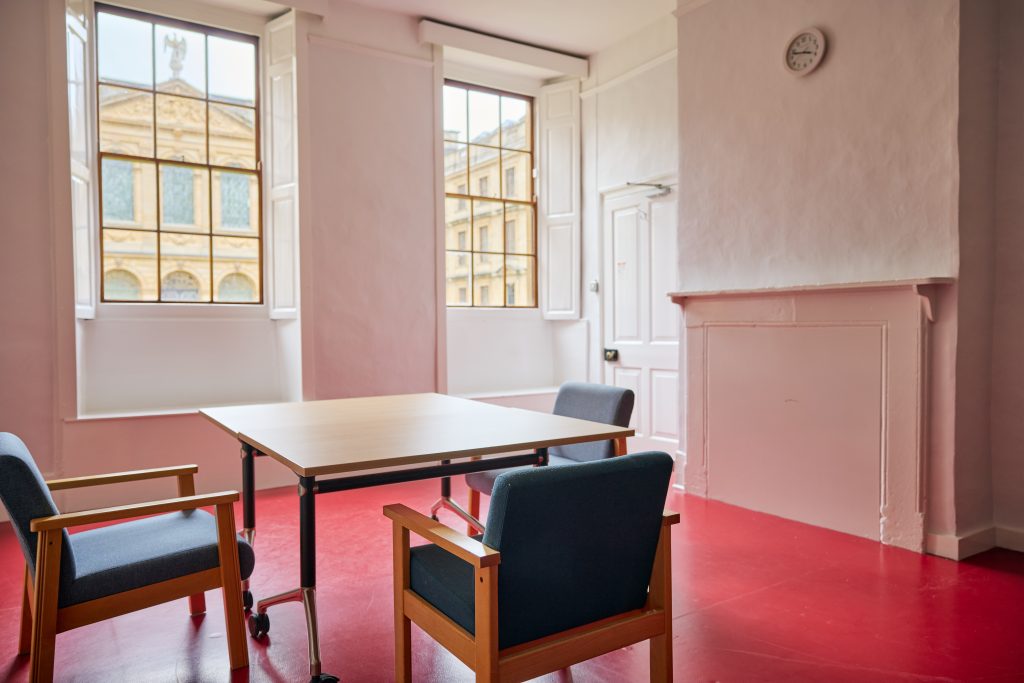 A room with a red floor and desk with three chairs around it