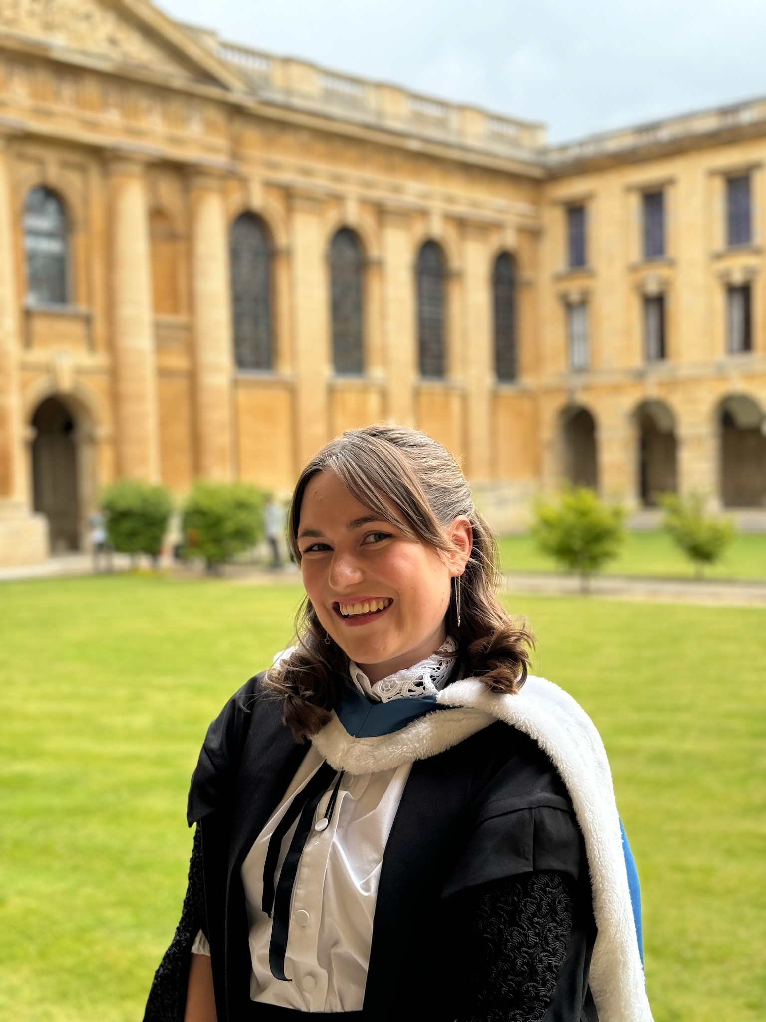 Becky Howitt wearing subfusc on her graduation day. She is standing in Front Quad with the lawn and buildings in the background.