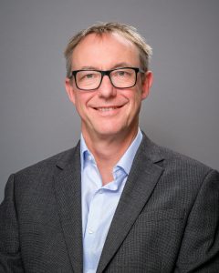 A profile photo of Paul Johnson wearing a grey suit jacket and a light blue shirt
