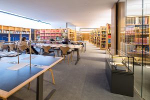 the main reading room showing desks on the left, an exhibition glass case on the right and bookshelves in the distance
