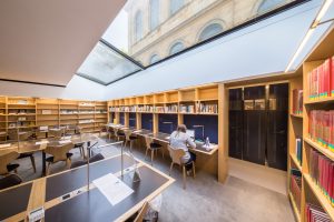 the main reading room in the New library showing desks, bookshelves and a view up to the Old Library through the skylight