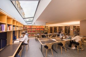 a wide angle view of the main reading room in the New library showing desks, bookshelves and a view up to the Old Library through the skylight