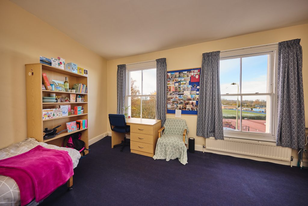 Cardo bedroom overlooking the University sports ground Cardo bedroom with bed, tall bookshelf, desk, chair and drawers, a comfy chair and two large window showing the running track across the road