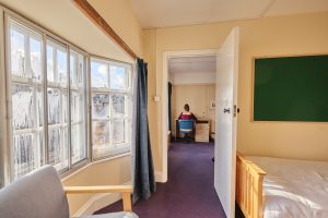 A student bedroom showing the ante room which contains a bed and through the door into the working area where a student sits at her laptop.