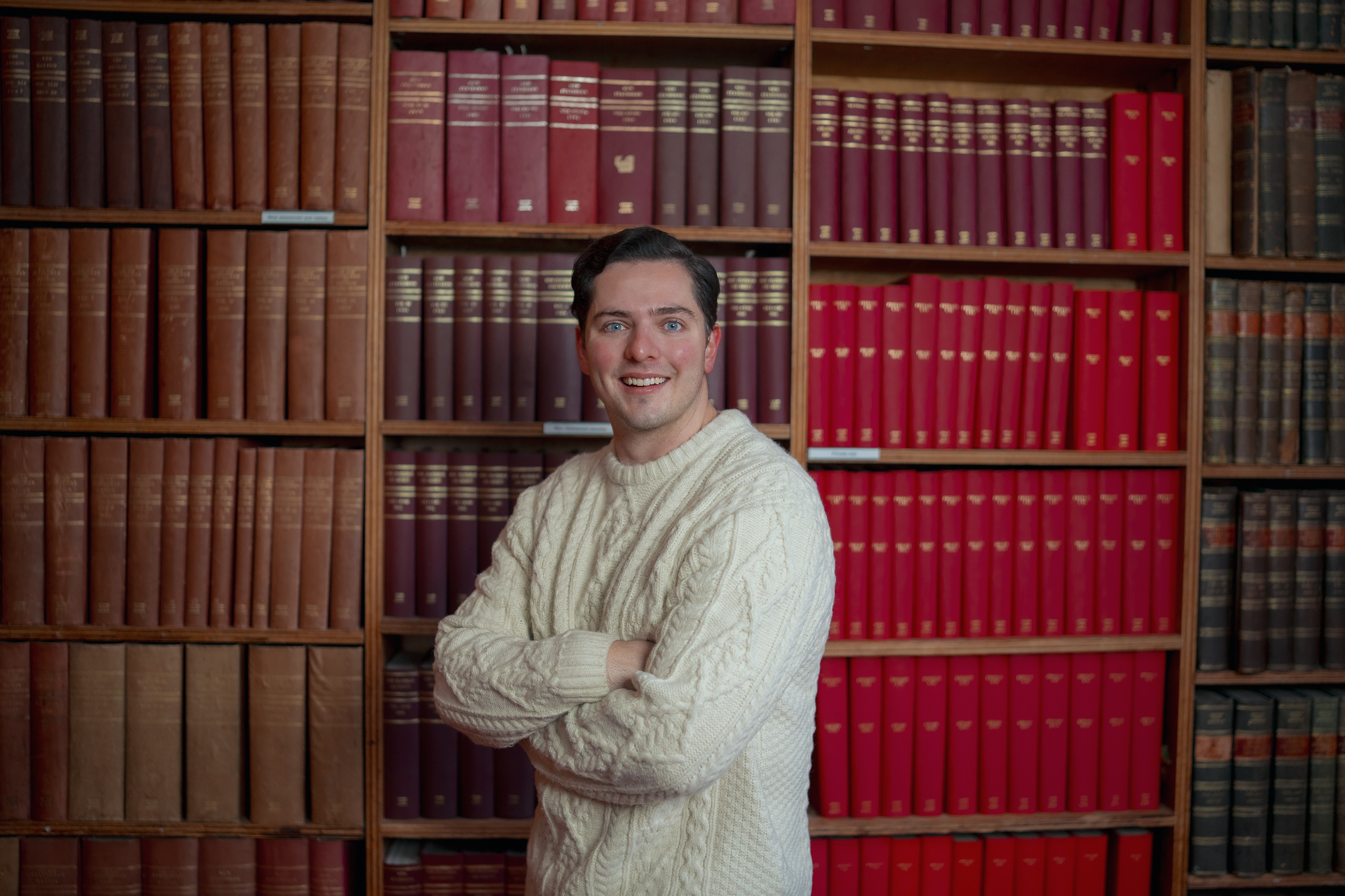 Matt Jarrett profile photo. Matt stands in front of a large bookcase containing old books.