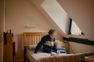 a student sits on a bed reading next to a slanted window