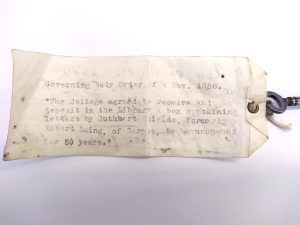 An old yellowing label attached to a key. The label reads: Governing Body Order of 4 November 1886: "The College agreed to receive and deposit in the Library a box containing letters by Cuthbert Shields, formerly Robert Laing, of Corpus, to be unopened for 50 years."
