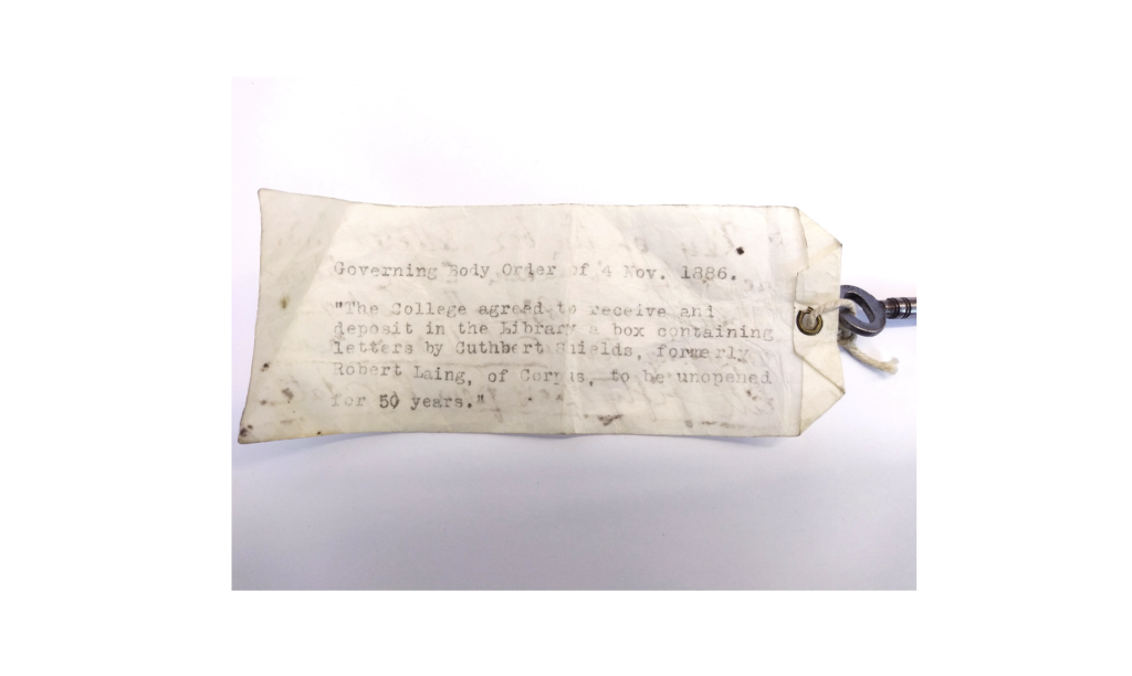 An old yellowing label attached to a key. The label reads: Governing Body Order of 4 November 1886: "The College agreed to receive and deposit in the Library a box containing letters by Cuthbert Shields, formerly Robert Laing, of Corpus, to be unopened for 50 years."