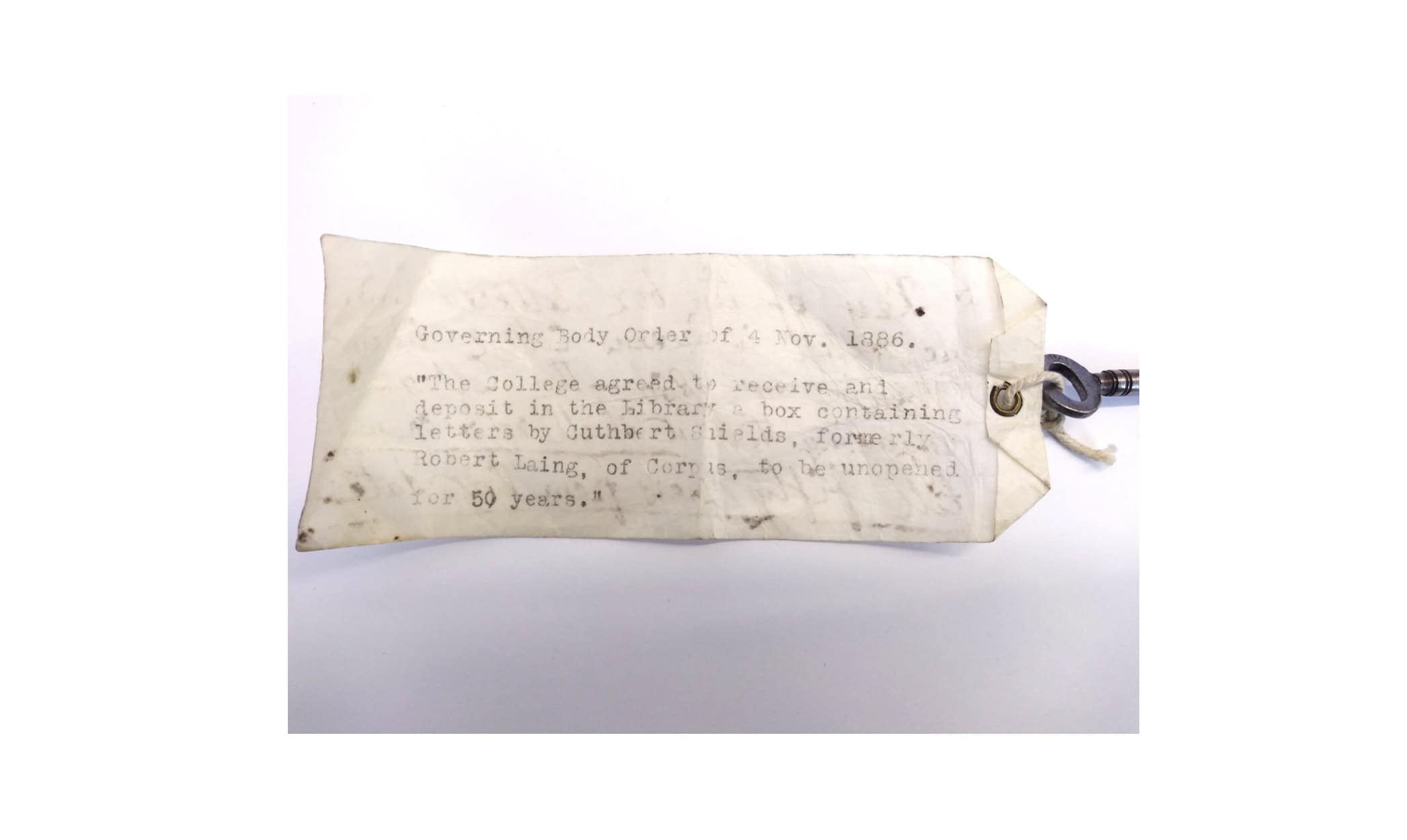 An old yellowing label attached to a key. The label reads: Governing Body Order of 4 November 1886: "The College agreed to receive and deposit in the Library a box containing letters by Cuthbert Shields, formerly Robert Laing, of Corpus, to be unopened for 50 years."