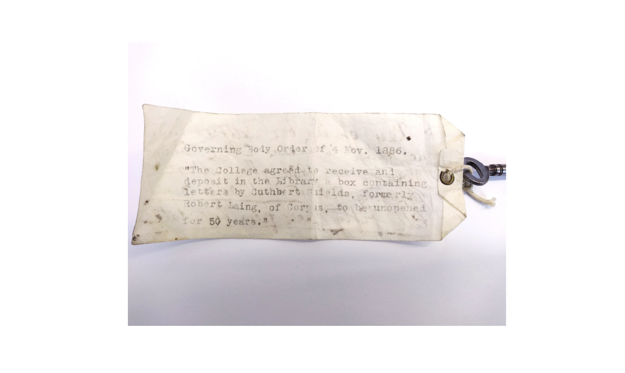 An old yellowing label attached to a key. The label reads: Governing Body Order of 4 November 1886: "The College agreed to receive and deposit in the Library a box containing letters by Cuthbert Shields, formerly Robert Laing, of Corpus, to be unopened for 50 years."