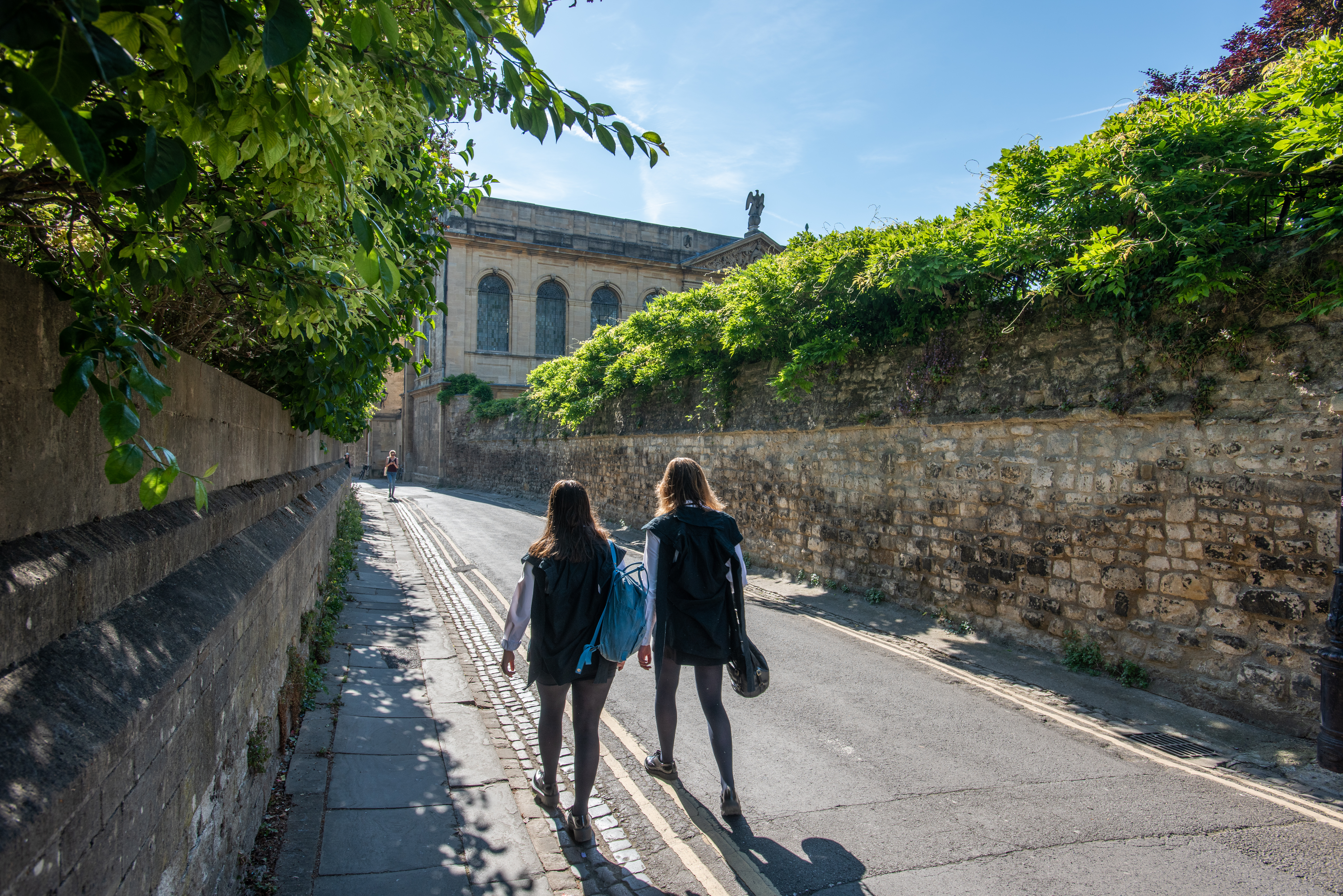 two students walking along Queen's Lane in subfusc, pictured from the back and looking towards Queen's library