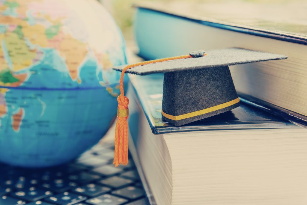 Graduation cap or hat, world globe map and foreign book on a laptop, depicts an achievement or success in long distant learning
