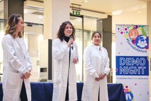 Olena Didenko pictured on demo night wearing a lab coat and speaking into a mic