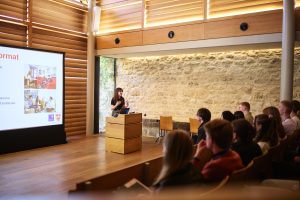 a plenary session for Science Residential attendees in the Shulman Auditorium. The photo is taken from behind a raked audience and towards a speaker at the lectern behind whom there is a presentation screen.