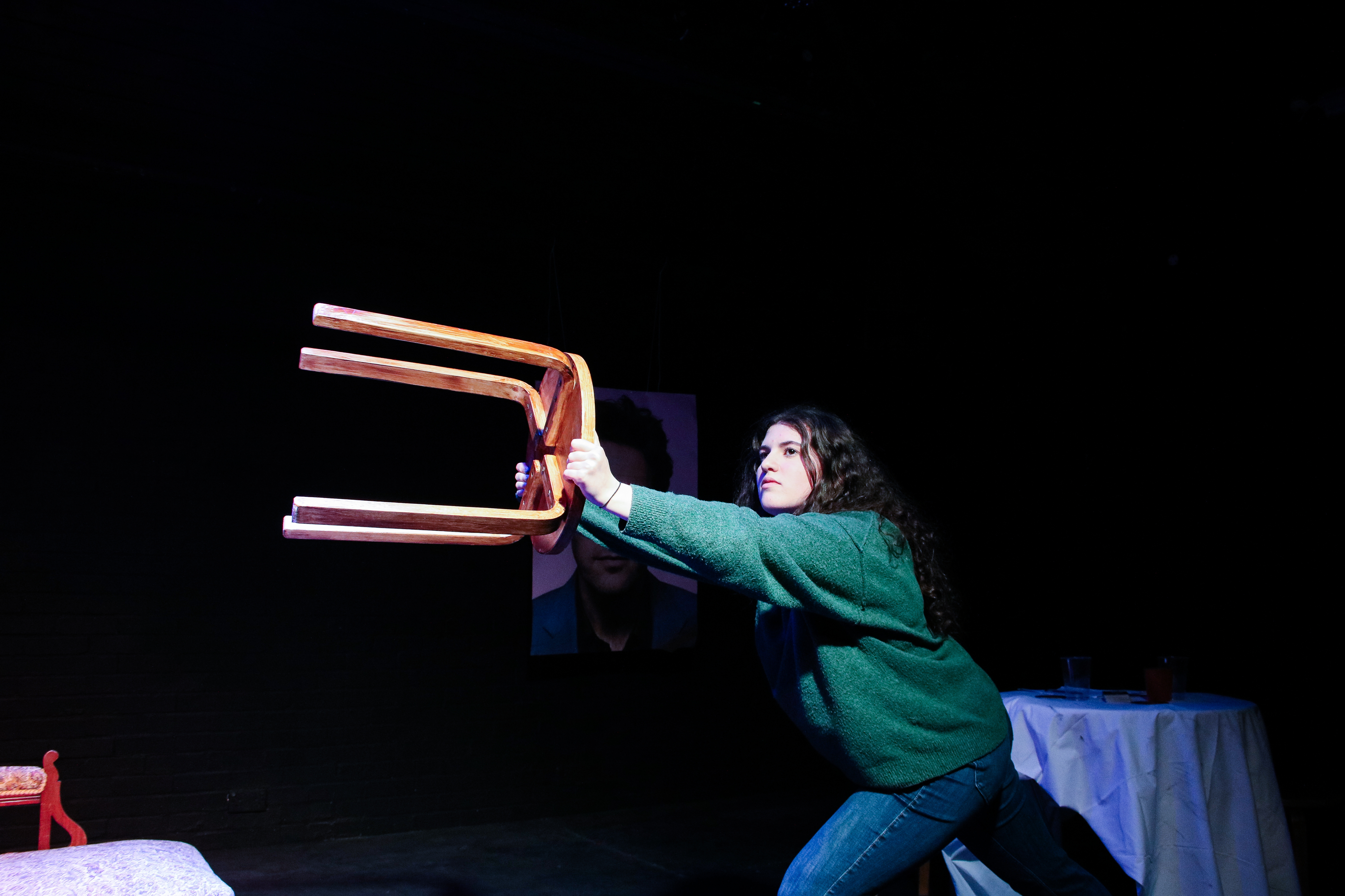 a photo from the production of Unprofessional that shows a person holding out a stool at arm's length against a black background