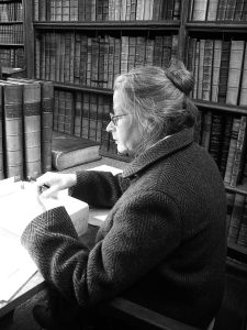 Helen Powell seated at a desk in the Upper Library with bookshelves visible behind her