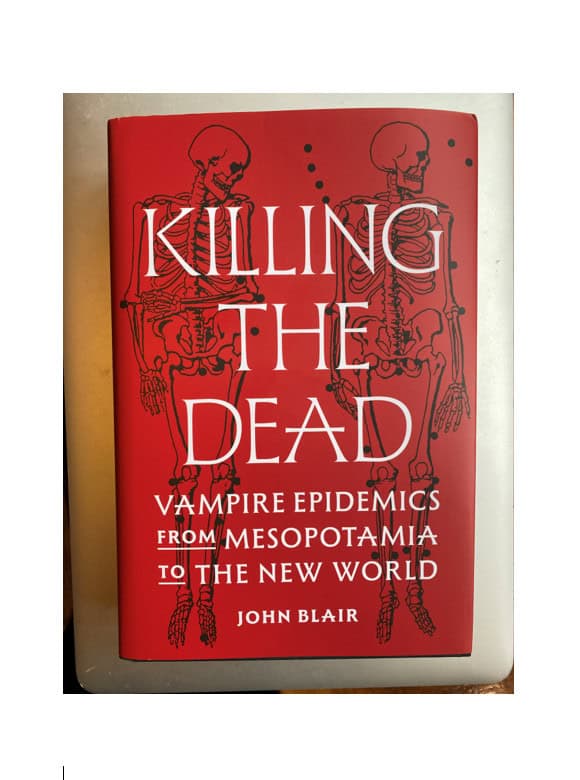 book cover of Killing the Dead. The background is red with two black skeleton drawings and title text in white. Sub-title and author text as follows: 'Vampire epidemics from Mesopotamia to the New World' by John Blair.