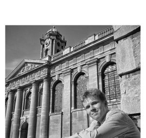 Danny McAlea sitting in Front Quad with the clock tower in the background