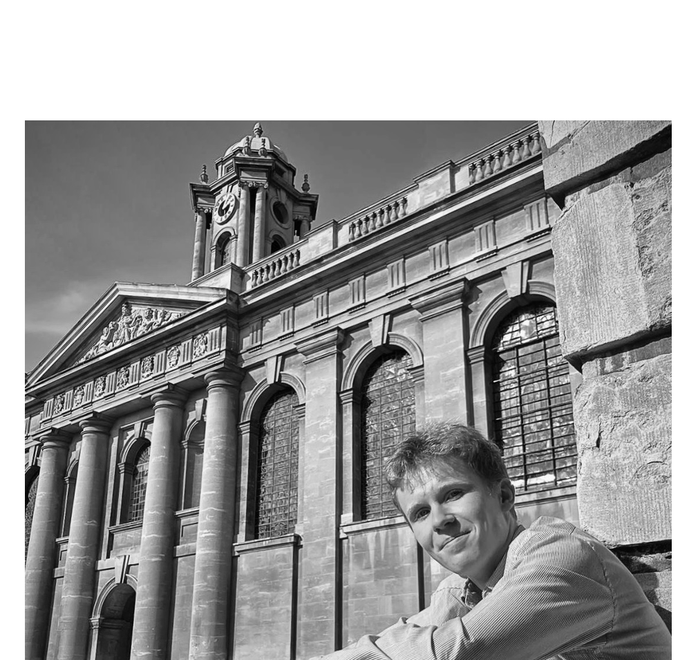 Danny McAlea sitting in Front Quad with the clock tower in the background