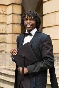 Tresor Nsengiyumva matriculation photo; he is wearing subfusc and standing in the Front Quad at Queen's
