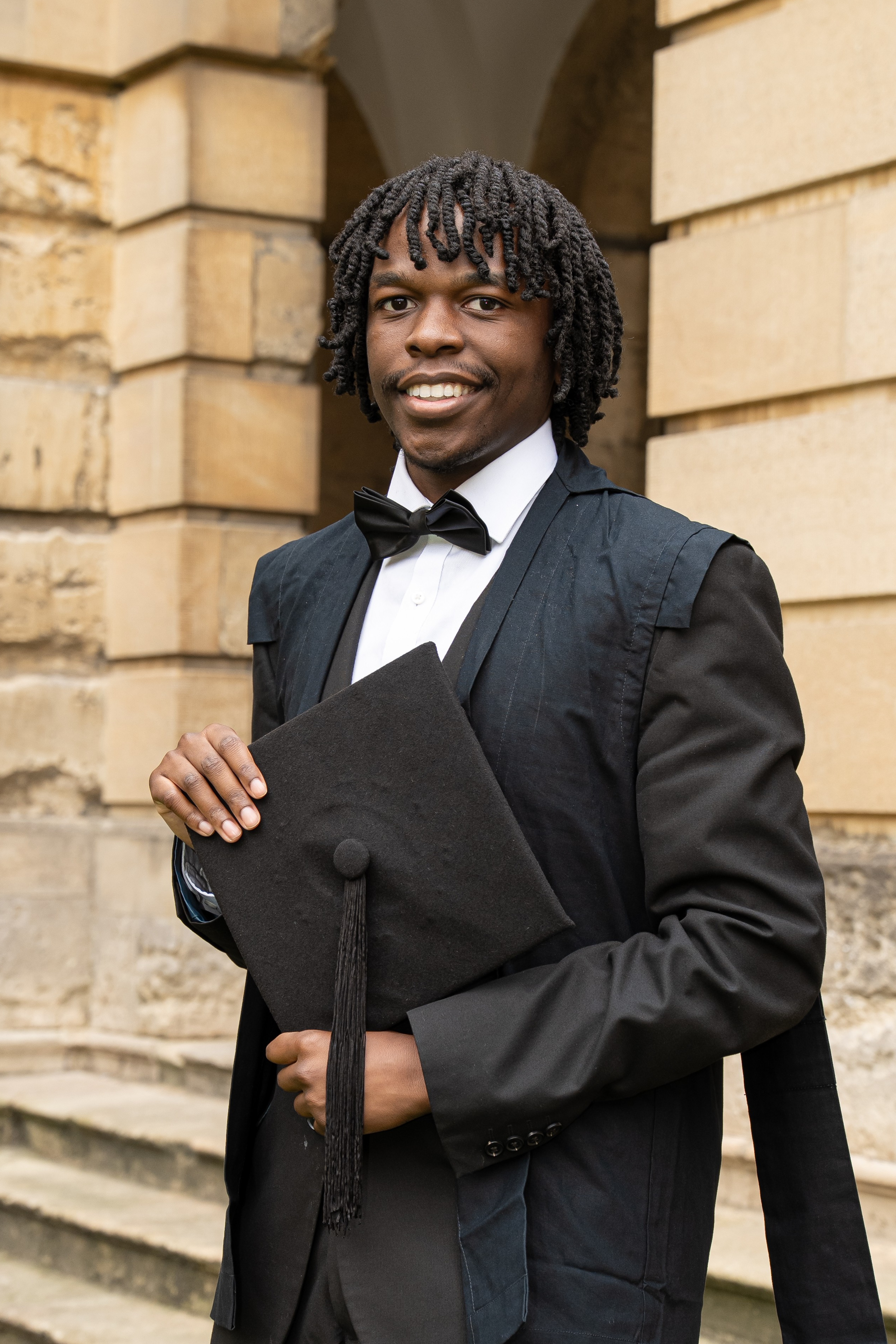 Tresor Nsengiyumva matriculation photo; he is wearing subfusc and standing in the Front Quad at Queen's