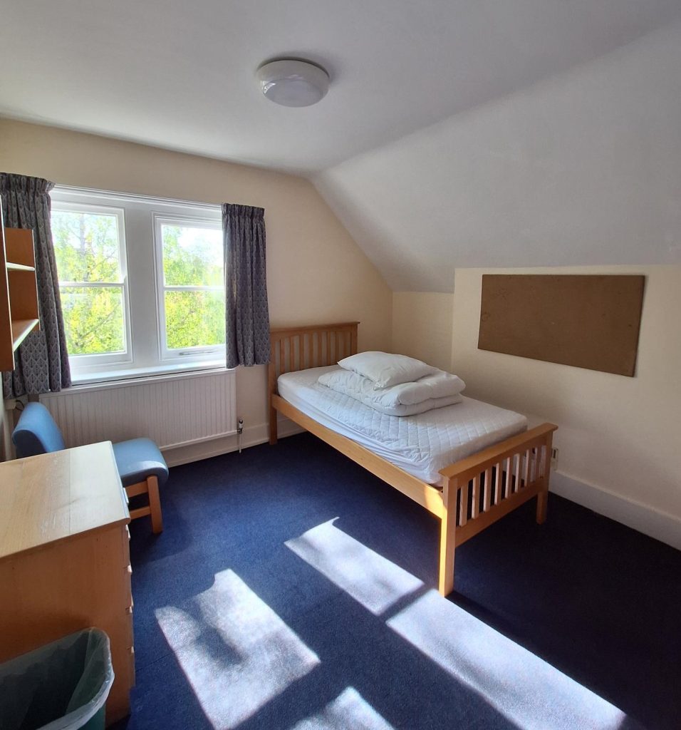 A bedroom with bed, chest of drawers, chair and window.