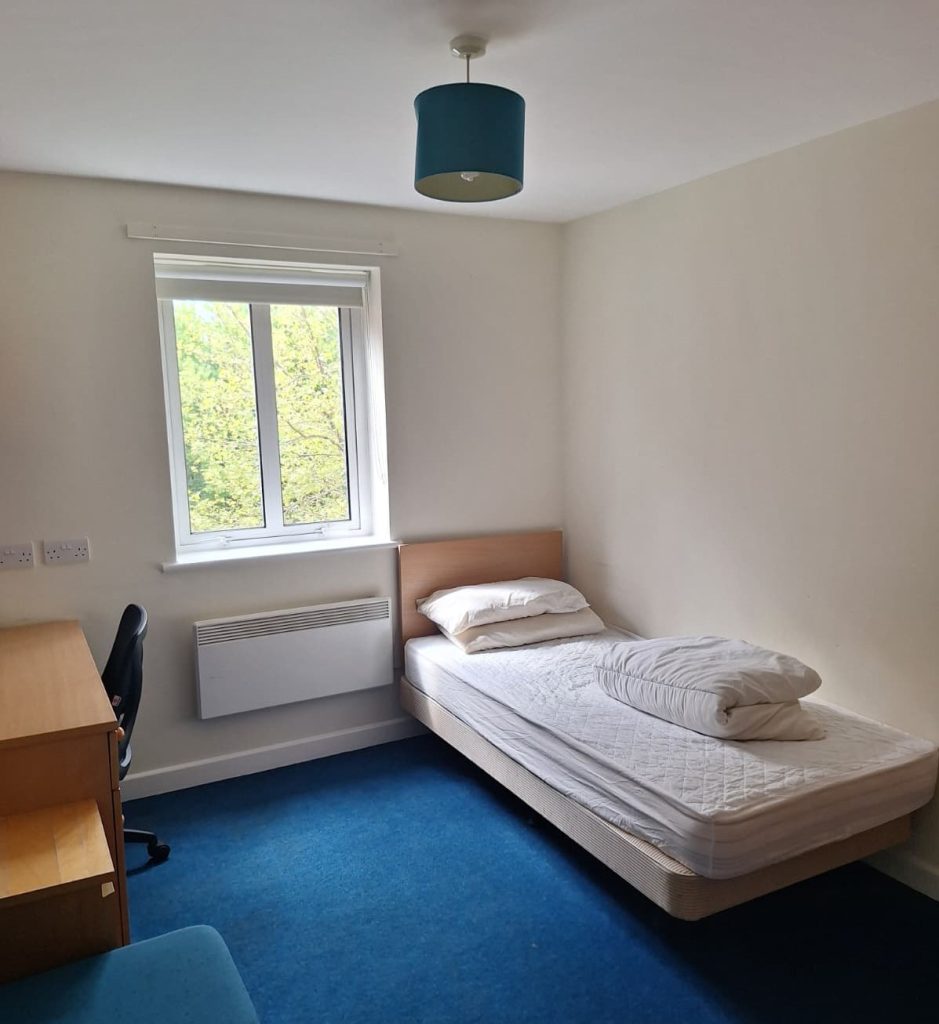 A bedroom with bed, desk, chair and window in the building on St Clement's.