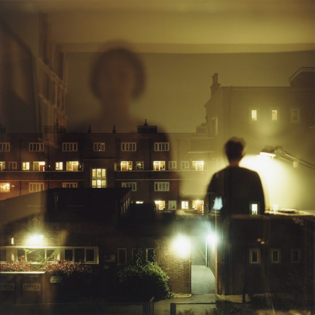 Photograph by Lydia Goldblatt showing overlapping images of a person looking out of a window and the surrounding buildings and windows: 'Windows', from the series 'Fugue'