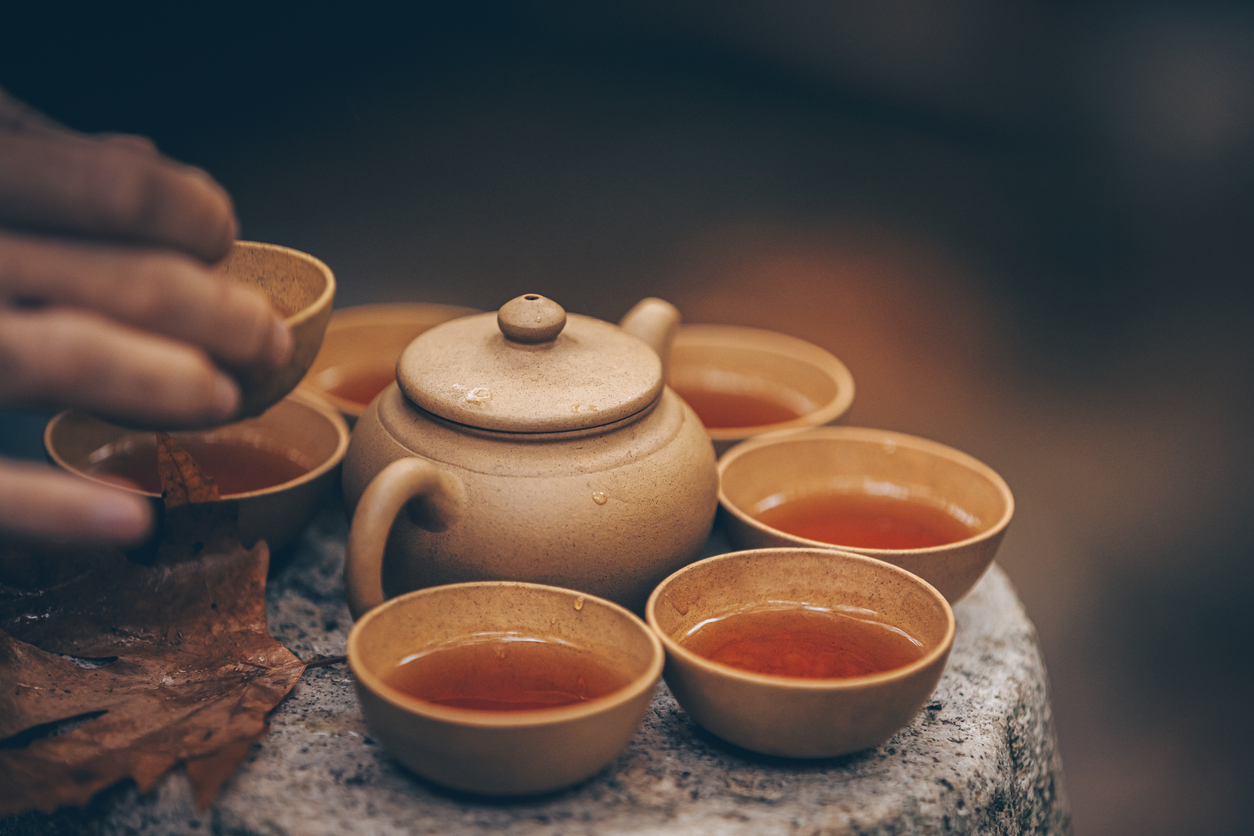 earthenware tea set resting on stone. a hand is just in view holding one of the cups which appear to contain tea.