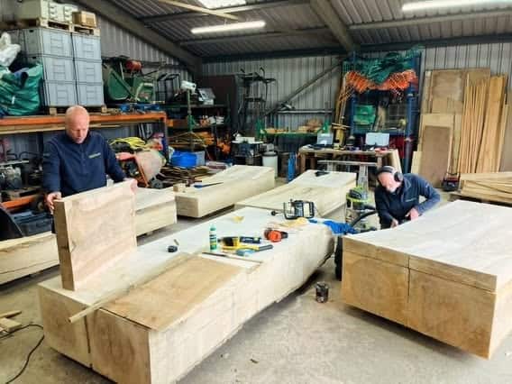 Two craftsmen working on large wooden furniture pieces in a workshop.