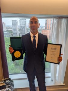 David Menassa pictured holding the Alumni Achievement Award.