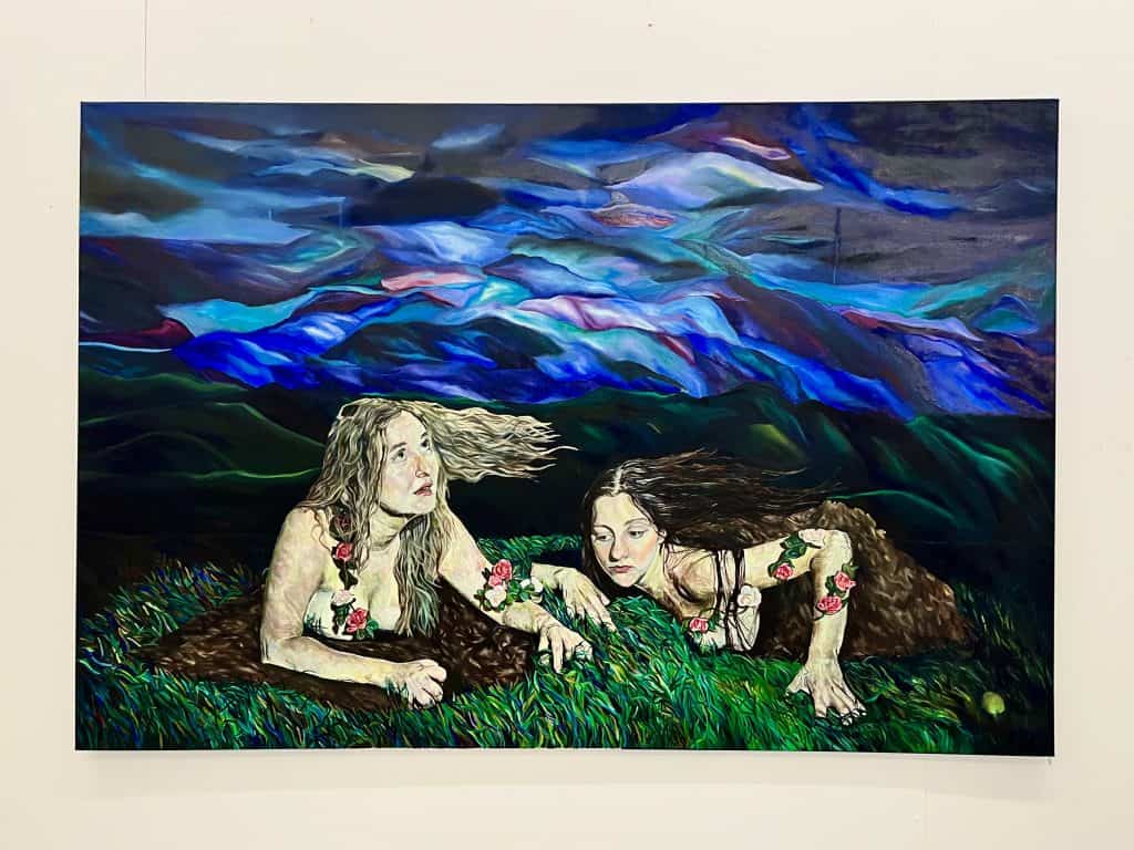 Born of the Loam, Daughters of the Horizon (oil on canvas) by Rosa Goddard; the painting depicts two women coming out of the ground. They are naked except for flower chains. The sky is dark and colourful, the ground is covered in grass and soil.
