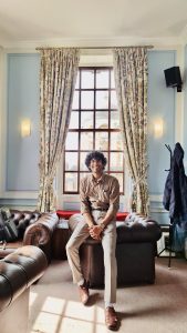 Parth pictured sitting on the arm of a leather sofa in the Middle Common Room