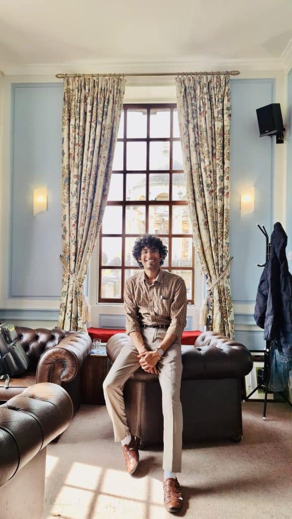 Parth pictured sitting on the arm of a leather sofa in the Middle Common Room