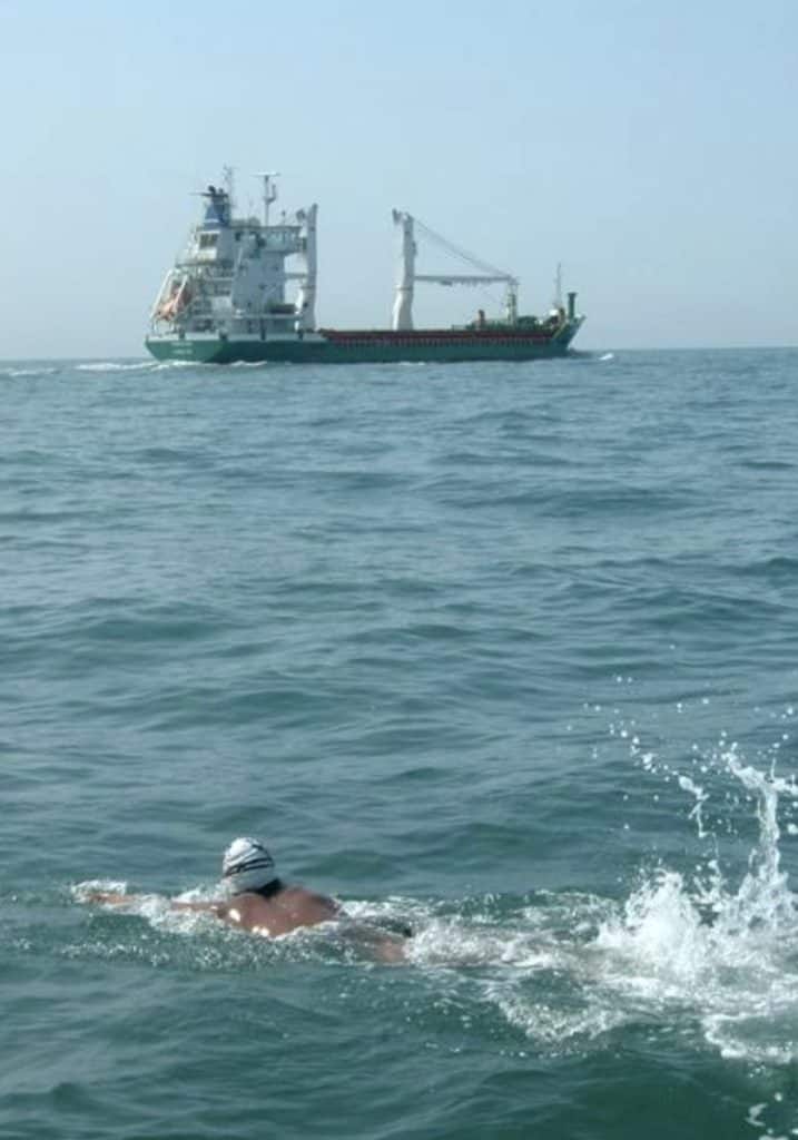 The image features a large ship sailing on the sea with a swimmer in the foreground