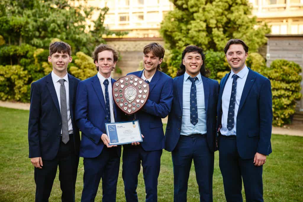 Group of five students in formal suits holding a shield and certificate